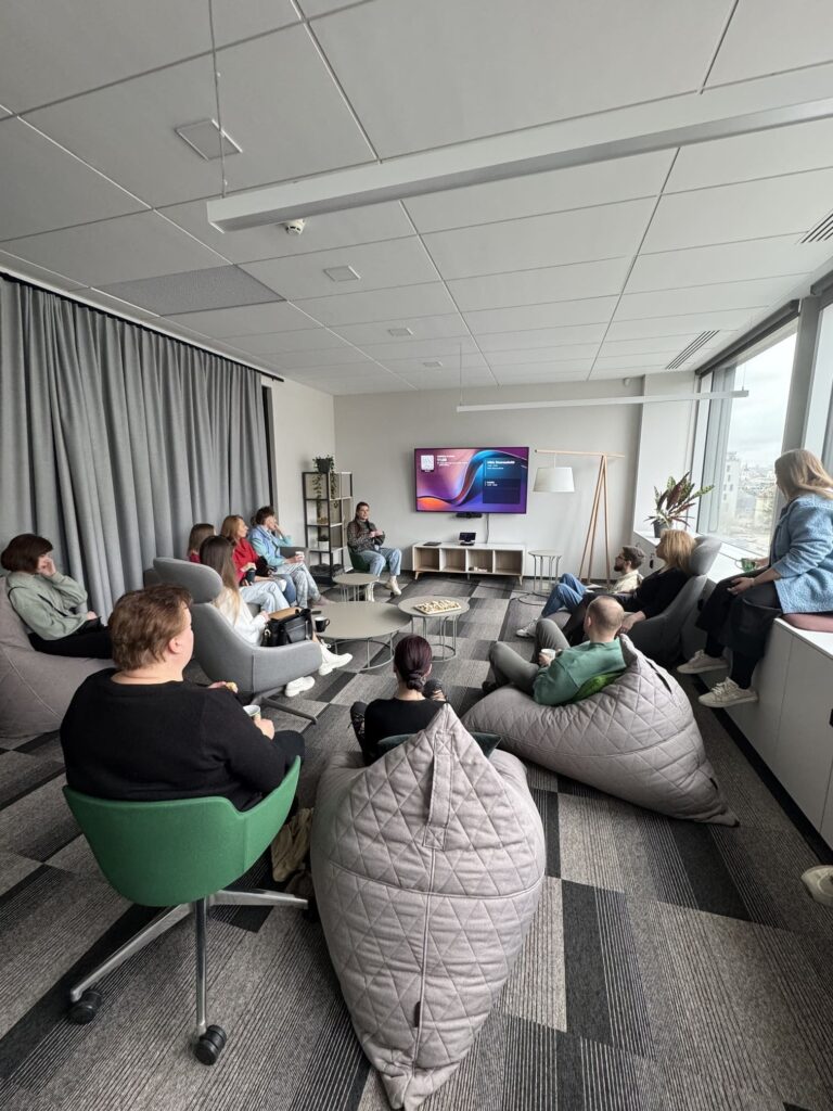 Nortal įmonės darbuotojai ir svečiai pristatymo metu poilsio zonoje. Draugiška darbo aplinka ir modernus biuras.