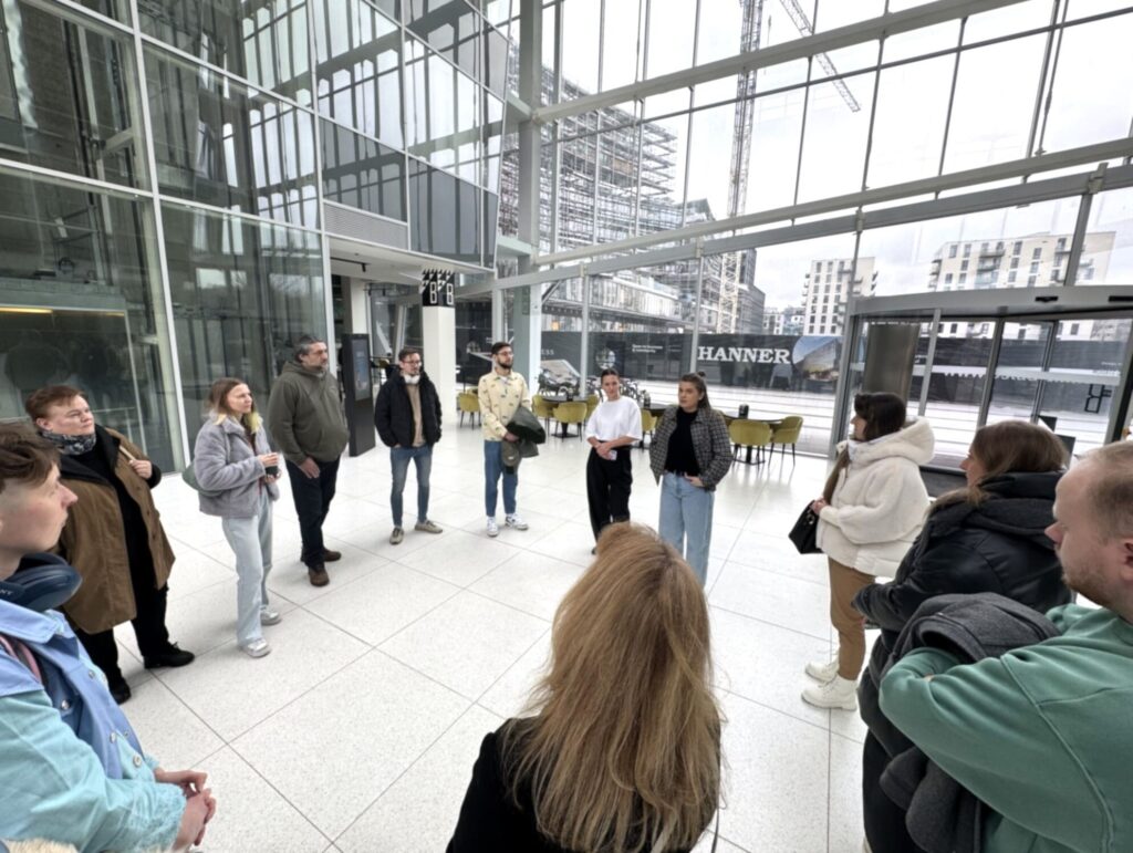 Nortal įmonės ekskursijos dalyviai susitikimo metu moderniame stikliniame vestibiulyje.